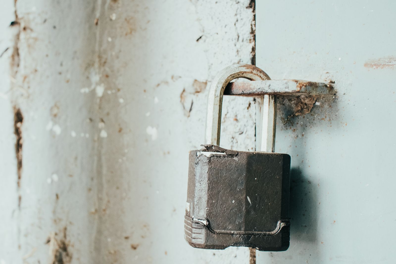 A rusty padlock hanging from a painted metal door